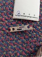 Close up photo of the silver tone initial pin with letters 'DSL' on a textured multicolor carpet surface