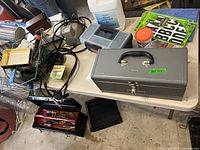 Overall view of table with toolboxes closed and open, hand sanitizer, tools, cords and other items scattered on table