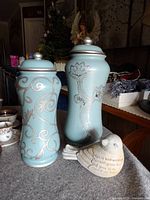 Two tall blue urns with floral patterns and lids, plus a stone bird figurine with inscription, displayed on a table.