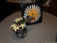 Canvas painting of a large flower on a 10-inch square black canvas, and metal balancing bird statue with white and yellow flowers and green leaves on a table.