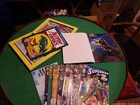 Comic books, poster page books, and framed posters displayed on a green round table.