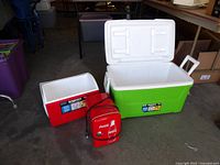 Photo showing large green and white Igloo cooler open beside smaller red and white Igloo cooler and Coca-Cola mini cooler in front.