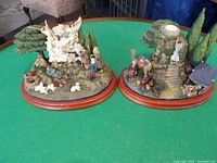 Photo of two Danbury Mint candle holder statues on green table showing the overall lot including wooden bases, figurines, and greenery.