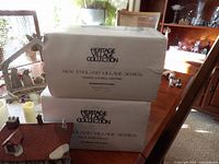 Stacked boxes labeled Heritage Village Collection, New England Village Series, with a ceramic house roof partially visible on the left.