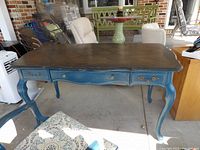 Desk shown from front with blue frame, scalloped edges, three drawers with brass hardware, and parquet wood inlay top.