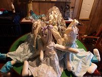 Photo showing three handmade cloth Easter bunnies in pastel floral dresses, sitting in front of a large wreath made of wooden and plastic eggs in various pastel colors.