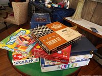 Stacked family board games showing Trouble, Yahtzee, Sequence, and The Game of Life with Chicken checker set on top