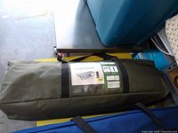 Green carrying bag containing folded hammock with stand, shown closed and zipped.