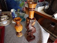 Front view of two wooden vases and one wooden figurine on a table with various background items.