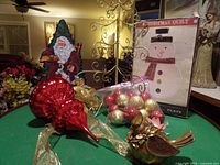 Photo of large red hand-blown glass ornament, metal ornamental tree, bag of Christmas ball ornaments, golden cardinal figurine, and Santa figurine