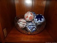 Large crystal bowl holding seven decorative ceramic or porcelain balls showing multiple floral and geometric patterns.