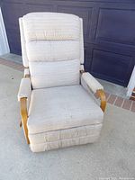 Front view of beige Lazy Boy recliner chair with wood armrests, padded backrest, seat, and visible tear at bottom of footrest upholstery.