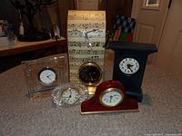 Lot showing all six clocks arranged on a table, featuring variety of styles and materials including glass, wood, and printed design.