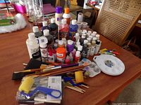 Overview of table with paint bottles, brushes, foam rollers, and palettes scattered on table