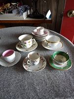 Overview of six porcelain teacups and their matching saucers arranged on a grey textured surface, showing different floral and decorative patterns.