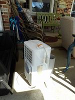 White portable air conditioner unit with power cord coiled attached, showing rear air vents and label.