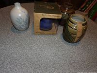 Photo of three items on a table: one white vase with blue leaf design, one brown and olive ceramic vase, and a boxed wind chime.