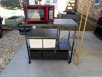 Side angled photo of the rolling cart with red microwave placed on top and five canvas bins on lower shelves.