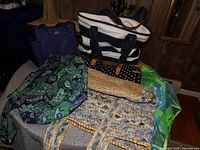 Tote bags arranged on a table showing different designs and colors, including striped black and white canvas, floral Vera Bradley, polka dot and straw bags.