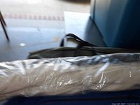 Photo of cream patio umbrella wrapped in a clear plastic cover, showing part of the patio space and some furniture in background.