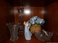Full view of lot items on wooden shelf including crystal vases, angel figurine, and woven basket with flowers