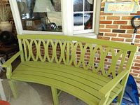 Front view of curved green wooden bench on patio showing slatted seat and back design
