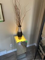 Mirrored rectangular prism table with illuminated top surface, plugged in and lit, holding brown-beige vase with decorative sticks