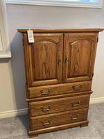 Full frontal view of oak wood armoire with double doors and three drawers beneath, showing brass hardware.