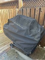 Grill covered with black Broil King cover on wooden deck