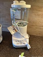 Full view of white KitchenAid blender with glass pitcher on kitchen counter showing cord and lid.