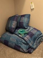 Folded queen size comforter with two matching pillow shams stacked in corner next to turquoise turtle dish
