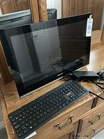 Asus all-in-one computer showing main unit, keyboard, wired mouse, and power cable with reflective screen.