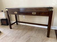 Front view of the console table showing brass corner trim and brass drawer pulls on center drawer.