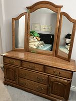Front view of the oak dresser with attached tri-fold mirror, showing brass hardware and wood grain finish.