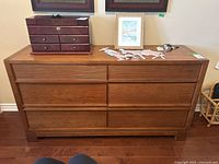 Front view of 6 drawer wood dresser with several items on top including a wooden jewelry box, decorative horse figures, a picture frame, and miscellaneous small items.