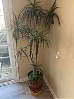 Full view of the tall faux floor plant showing multiple stalks and leaves near a window corner.