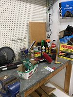 Photo of garage workbench countertop with assorted automotive and cleaning products, clock, brush, and small tools on pegboard wall