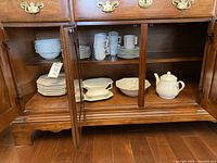 Wooden cabinet open showing stacked white octagonal dishes on lower shelves including plates, bowls, gravy boat and teapot
