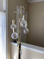 Full view of brass floor lamp showing all five arms and glass globe bulbs