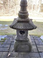 Front view of 32-inch tall cement outdoor pagoda on stone patio, showing decorative tiled roof and weathered surface.