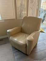 Front and side view of beige leather recliner showing cushioned arms and seat with wear on the arms.