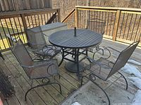 Overview of the round cast iron patio table set outdoors on a deck, showing the table and four chairs with cushions.