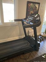 Side view of black Xterra XT900 fold-up treadmill showing running belt and basic structure in room with window.