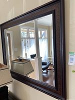 Full view of the mirror hanging on a wall, showing the beveled mirror surface and patterned frame in a home setting.