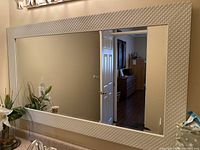 Full view of large rectangular beveled mirror mounted on wall reflecting hallway and other rooms.