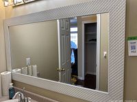 Full view of the rectangular wall mirror mounted on a beige wall above a countertop with bathroom essentials visible.