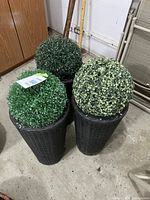 Overview of three black wicker conical plant stands each topped with a faux greenery sphere