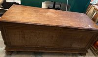 Front view of the antique cedar chest, showing the wood grain and paneled design with signs of wear and scratches.