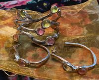 Free form cast wax cuff bracelet and matching earrings on a fabric background, showing multicolored cabochons in a twig-like silver-toned design.
