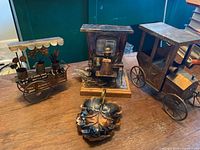 Four copper decor pieces on wooden surface including flower cart, jalopy, piano player, and leaf dish.